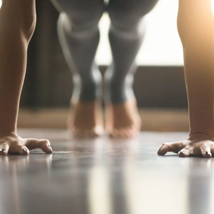 Young woman practicing yoga, doing Push ups or press ups exercise, phalankasana Plank pose, working out, wearing sportswear, grey pants, indoor, home interior, living room floor. Close-up of hands